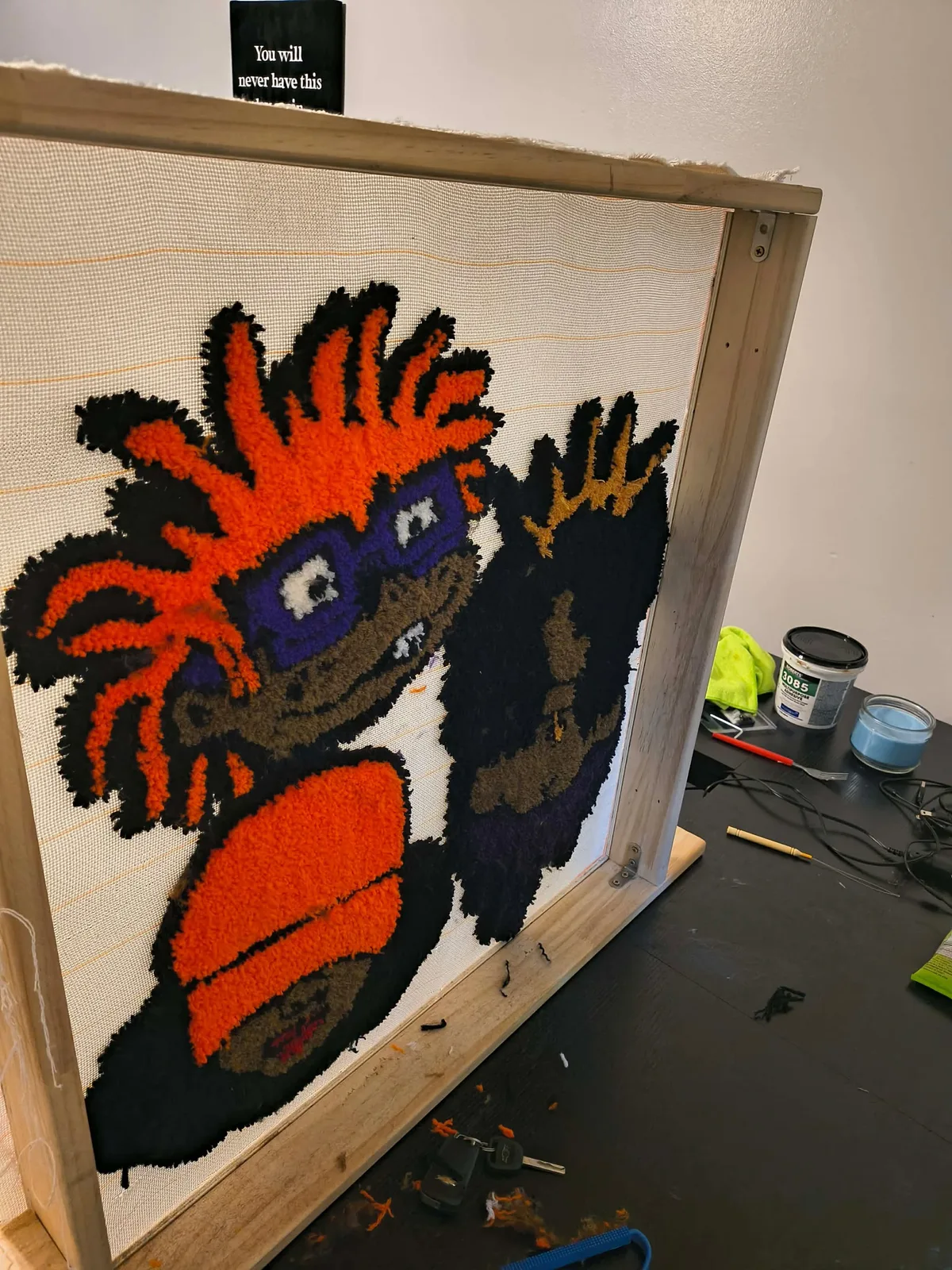 A character design part-way through tufting, stretched on a wooden frame with the undyed cloth still showing.